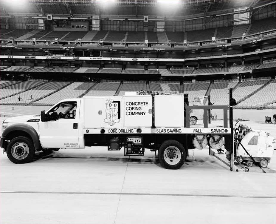 Concrete Coring Company slab sawing truck parked on the field of an empty Phoenix stadium, saws loaded across the bed